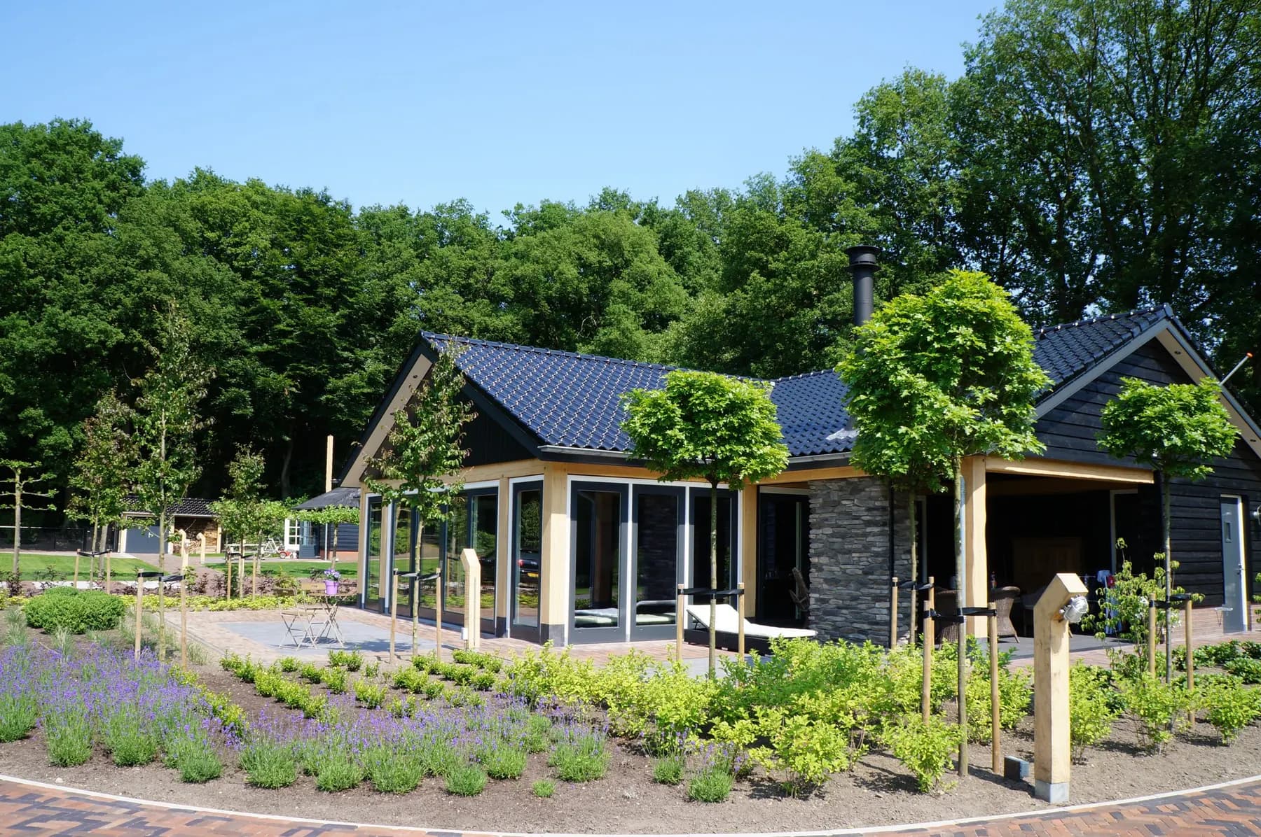 Vrijstaand wellnessgebouw met zwart pannendak en glazen gevels, opgeleverd met aangelegde tuin