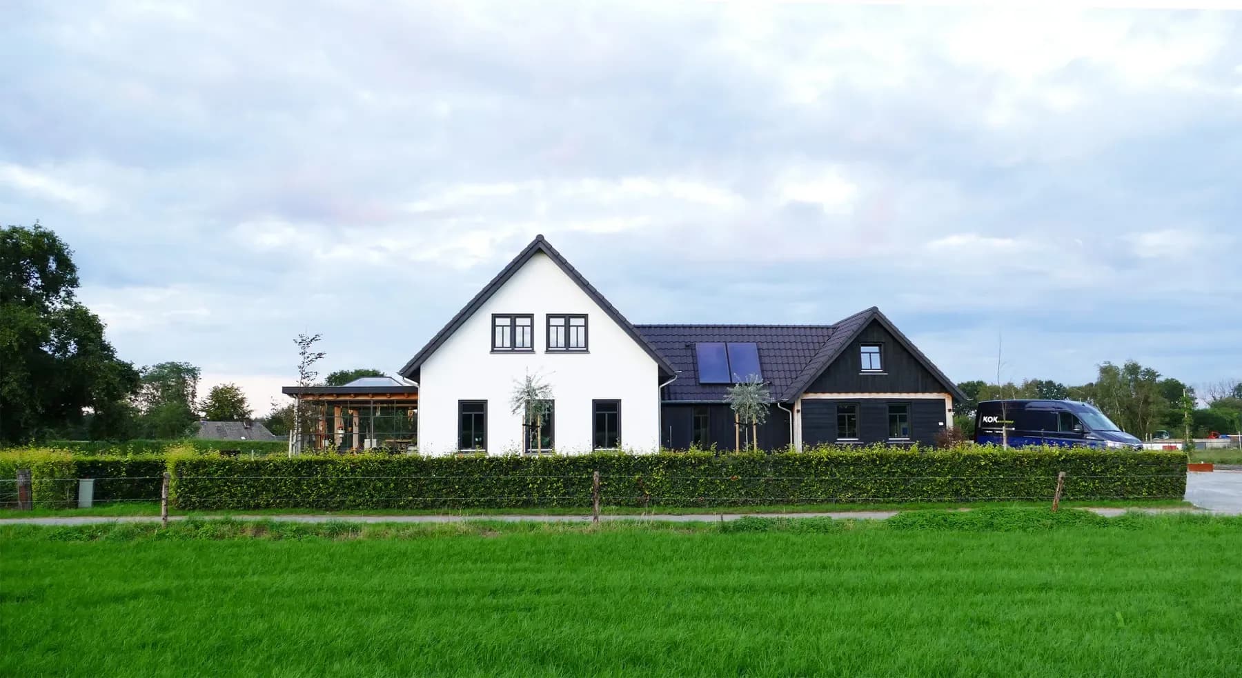 Wit gestucte nieuwbouwwoning met zonnepanelen in het dakvlak, gezien vanaf het weiland